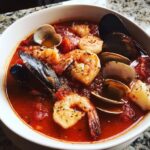 Close-up of a hearty bowl of seafood soup cioppino featuring shrimp, mussels, clams, and scallops in a rich tomato broth.