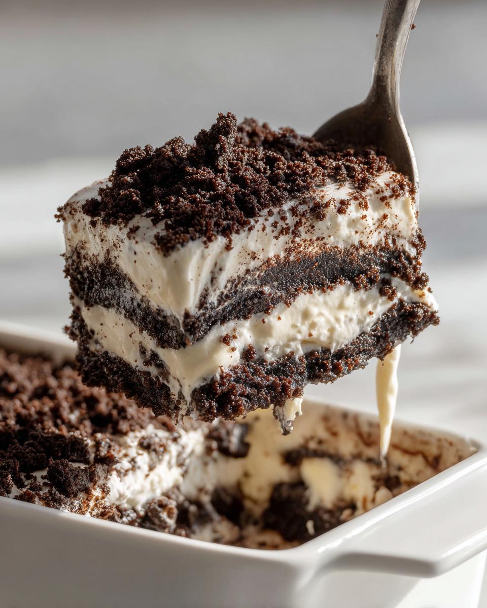 A spoonful of layered Oreo dirt cake being lifted from a white dish, showing creamy filling and cookie crumbs.