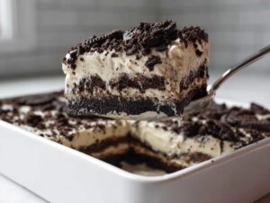 A spoonful of creamy, layered Oreo dirt cake being lifted from a white dish.