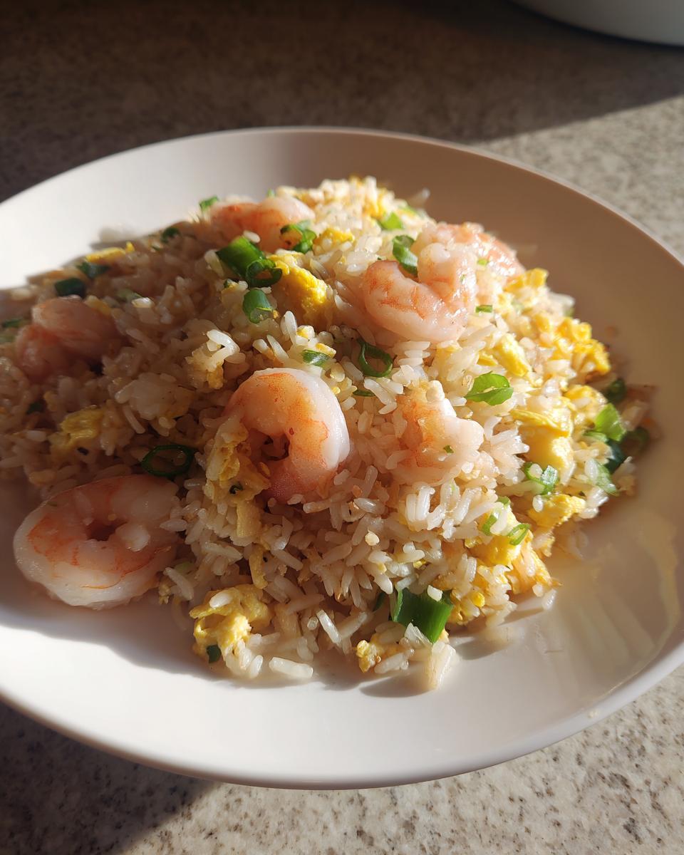 A close-up serving of delicious shrimp fried rice recipe with visible shrimp, scrambled egg, and green onions.