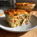 A generous slice of turkey pot pie with flaky crust and creamy filling, served on a white plate.
