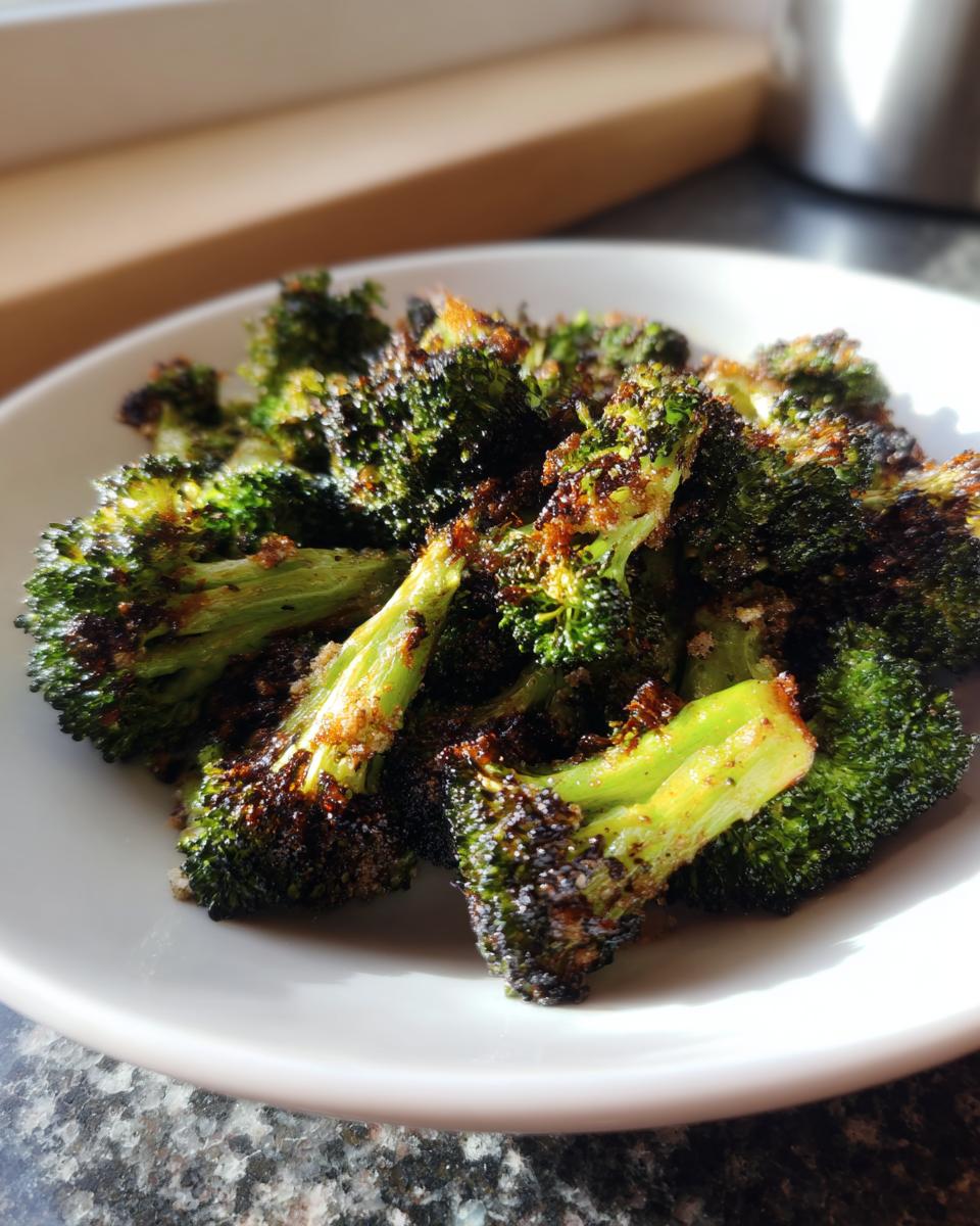 Close-up of crispy, charred smashed broccoli florets served on a white plate, highlighting the texture.