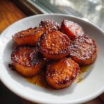 Close-up of perfectly glazed, round slices of southern candied yams resting in a white bowl.