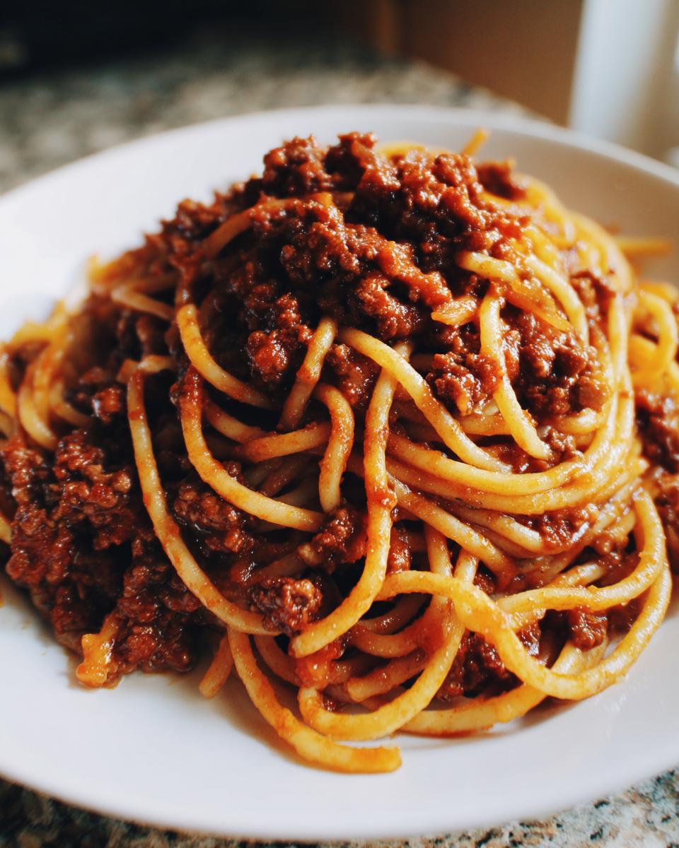 Close-up of spaghetti generously topped with rich, slow-cooked bolognese sauce on a white plate.
