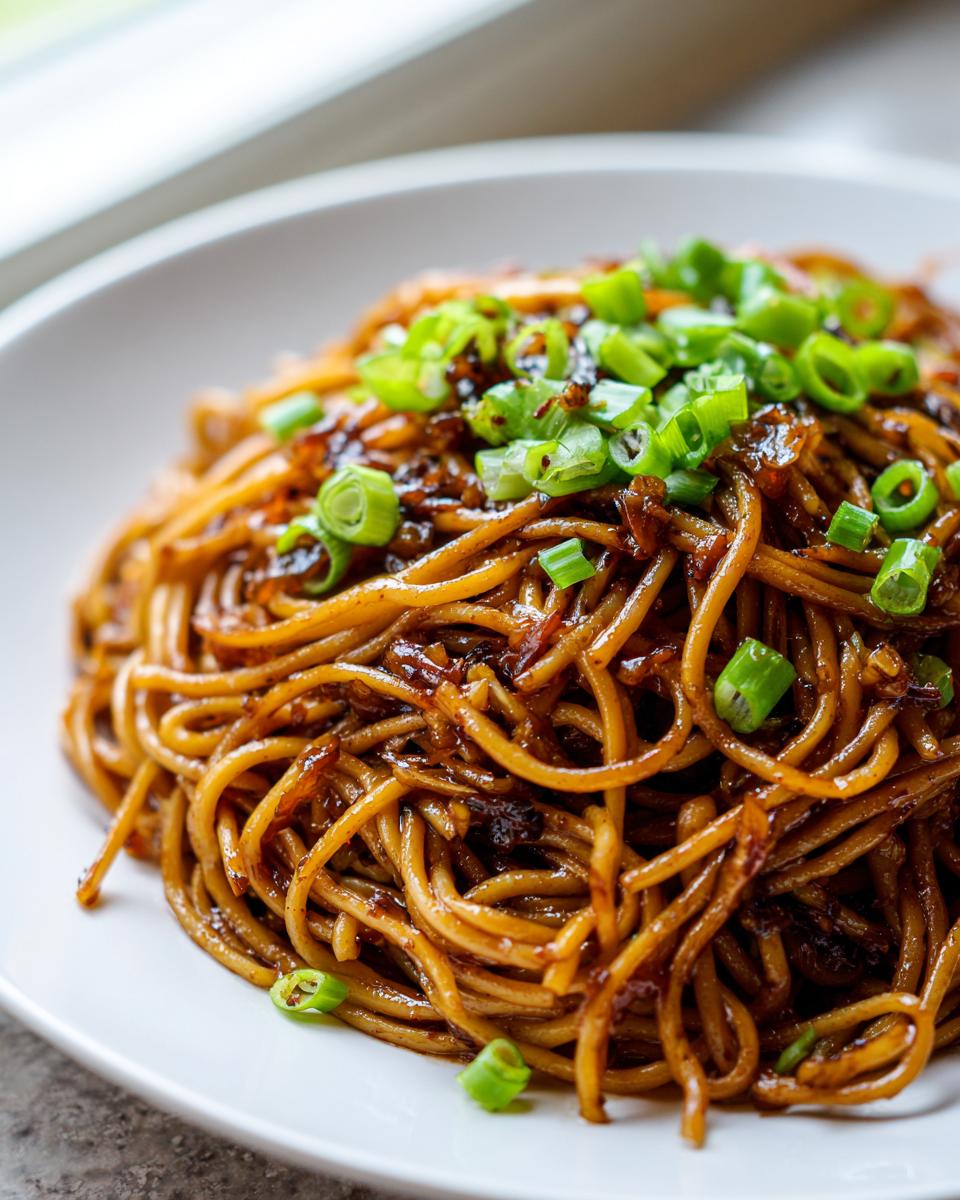 A close-up of glossy, saucy garlic noodles topped generously with fresh chopped green onions.