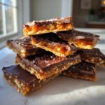A stack of rich saltine cracker toffee squares topped with melted chocolate and flaky sea salt.