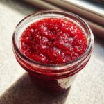 Close-up of a glass jar filled with vibrant red strawberry freezer jam, showing texture and seeds.