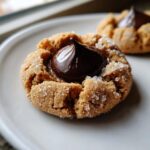 A close-up shot of a perfectly baked peanut butter blossom cookie rolled in sugar with a melted chocolate kiss center.
