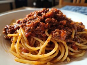 Close-up of spaghetti noodles generously topped with rich, thick bolognese sauce in a white bowl.