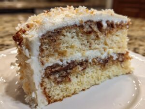Close-up of a moist slice of white German chocolate cake layered with coconut-pecan filling and white frosting.