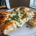 A hand pulling a cheesy slice away from a homemade white pizza topped with melted cheese and fresh parsley.