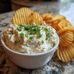 Creamy clam dip topped with fresh green onions, served with a ruffled potato chip for dipping.