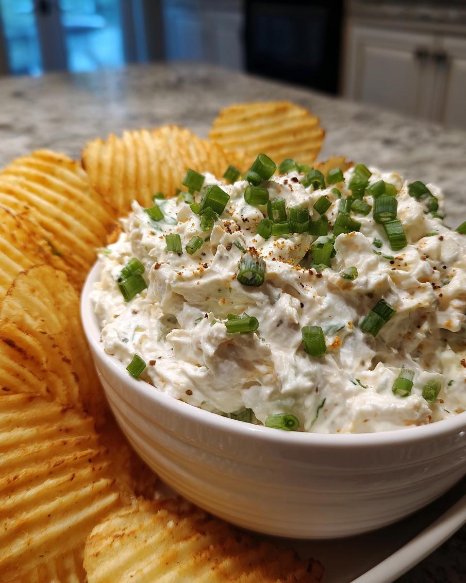 A creamy bowl of amazing 10 minute clam dip topped with chopped green onions and served with ruffled potato chips.