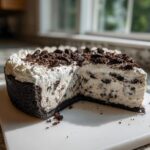 A slice removed from a creamy cookies and cream ice cream pie with a dark chocolate crust.
