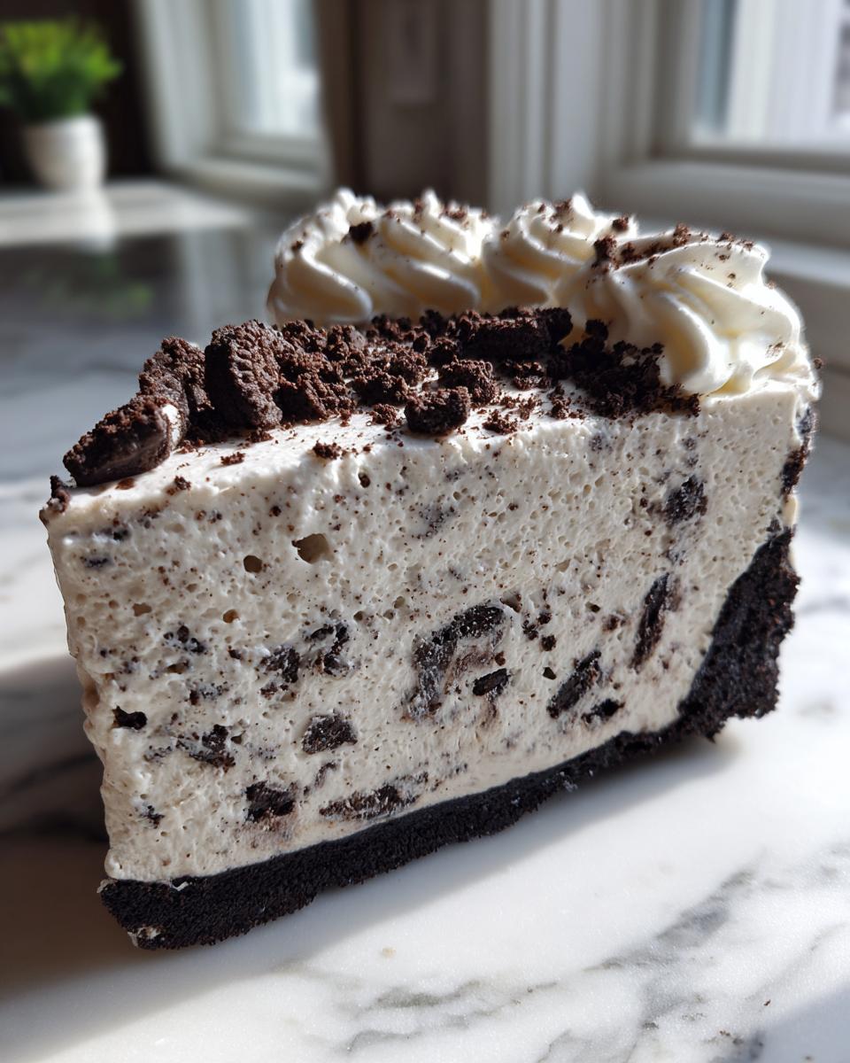 A tall slice of cookies and cream ice cream pie with a dark chocolate crust, topped with whipped cream.
