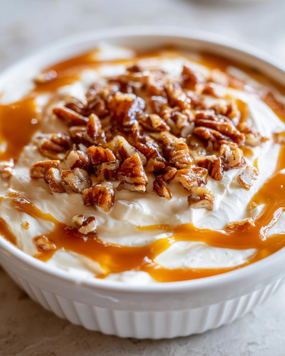 A close-up of creamy pecan pie dip topped with candied pecans and caramel drizzle.
