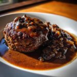 A close-up of a perfectly seared salisbury steak smothered in thick, rich brown onion gravy.