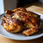 A whole, perfectly roasted spatchcock chicken with golden-brown, herb-crusted skin resting on a white plate.