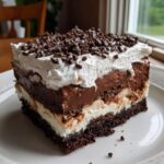 A rich, layered slice of brownie refrigerator cake featuring chocolate mousse, cream, and mini chocolate chips on top.