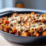 Close-up of a savory sweet potato skillet topped with melted cheese, ground meat, and black beans.