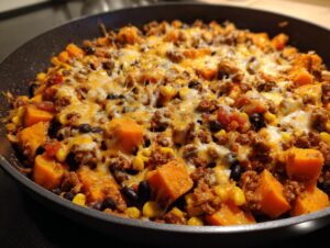 Close-up of a savory sweet potato skillet topped with melted cheese, ground meat, black beans, and corn.