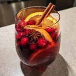 A chilled glass filled with dark red holiday sangria, garnished with fresh cranberries, orange slices, cinnamon sticks, and star anise.