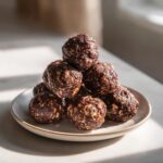 A pyramid stack of rich, dark chocolate protein balls made with visible oats, sitting on a small ceramic plate.