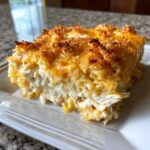 A close-up of a square serving of creamy chicken noodle casserole with a golden, cheesy, and crunchy topping.