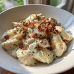 A close-up of creamy crack chicken gnocchi in a white bowl, topped generously with crispy bacon bits and fresh chives.