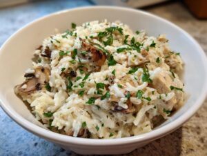 Close-up of a creamy one pot chicken and rice dish topped with fresh parsley in a white bowl.