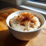 A white bowl filled with creamy rice pudding, generously topped with ground cinnamon.