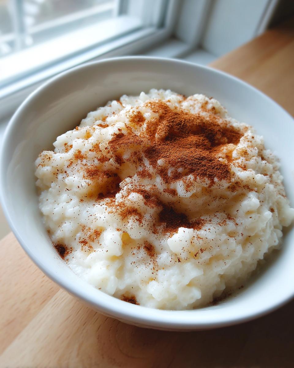 Close-up of creamy rice pudding in a white bowl, generously sprinkled with ground cinnamon.