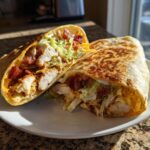 A crispy chicken bacon ranch wrap cut in half, showing layers of chicken, bacon, lettuce, and ranch dressing.