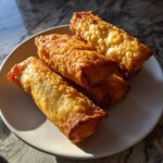 A stack of four golden brown, perfectly crispy fried egg roll appetizers resting on a light-colored plate.