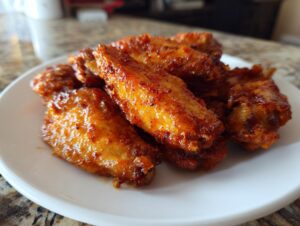 Close-up of several perfectly crispy, glazed chicken wings piled on a white plate.