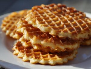 A close-up stack of golden brown, crispy pizzelle cookies resting on a white plate.