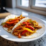 Two soft tortillas filled with seasoned shredded chicken and colorful bell peppers for crockpot chicken fajitas.