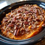 Close-up of a rich crockpot sweet potato casserole topped generously with whole and chopped pecans.