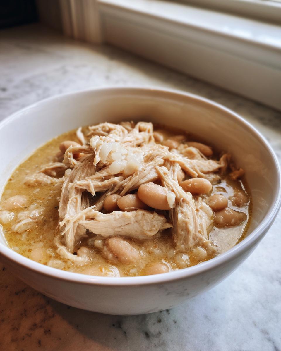 Close-up of a white bowl filled with hearty crockpot white chicken chili featuring shredded chicken and white beans.