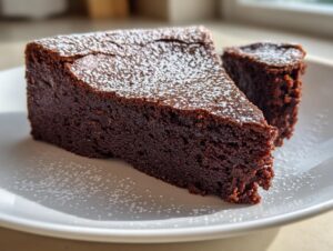 A rich, dark slice of flourless chocolate cake dusted with powdered sugar on a white plate.