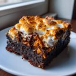 A single, fudgy hot chocolate brownie topped with perfectly toasted marshmallows, resting on a white plate.