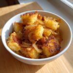 Close-up of golden brown fried potatoes cubes mixed with caramelized onions served in a white bowl.