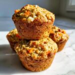A stack of three golden brown morning glory muffins featuring visible shreds of carrot and coconut.