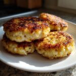 Four perfectly pan-fried salmon cakes stacked and resting on a white plate, showing a crispy golden crust.