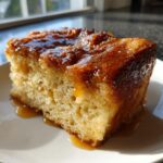 A close-up of a moist slice of apple bread pudding topped with a shiny, thick caramel glaze.