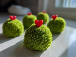 Close-up of several bright green, textured grinch oreo balls, each topped with a small red candy heart.