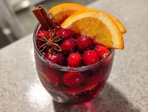 Close-up of a glass of rich red holiday sangria garnished with fresh cranberries, orange slices, star anise, and a cinnamon stick.