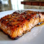 Close-up of a perfectly cooked salmon fillet glazed with honey garlic butter, resting on a white plate.