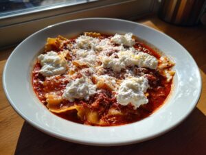 A white bowl filled with rich, red Instant Pot Lasagna Soup topped with dollops of ricotta and grated Parmesan cheese.