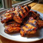 Close-up of several pieces of grilled chicken thighs showing char marks, coated in a sticky glaze from the chicken marinade.